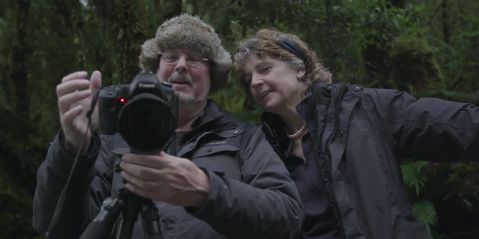 A man and woman look at a camera together