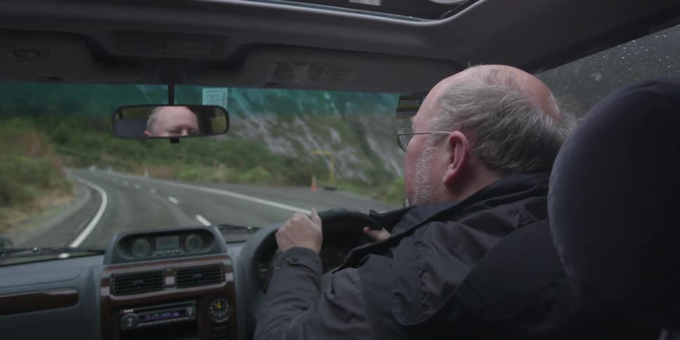 Balding man driving a car down a road