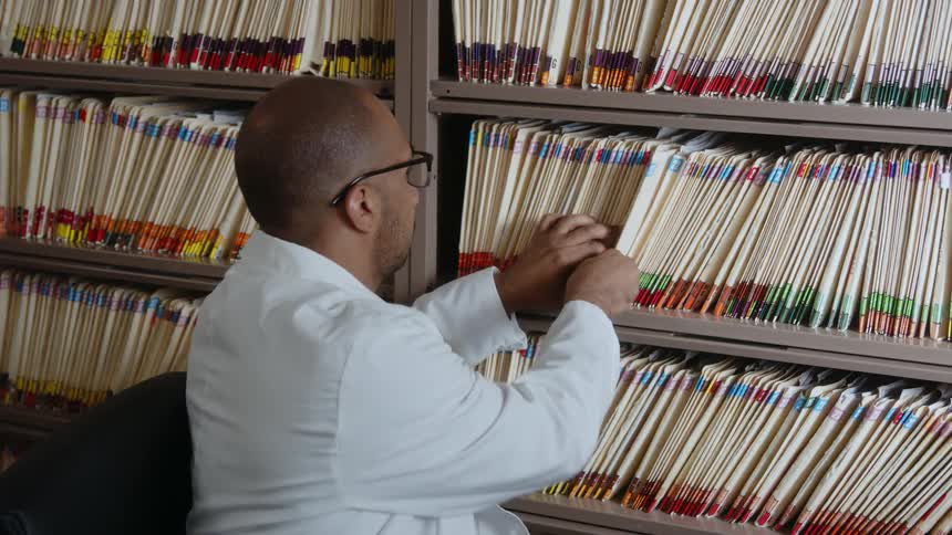A male doctor turning in his chair placing a file on the shelf and then turning back