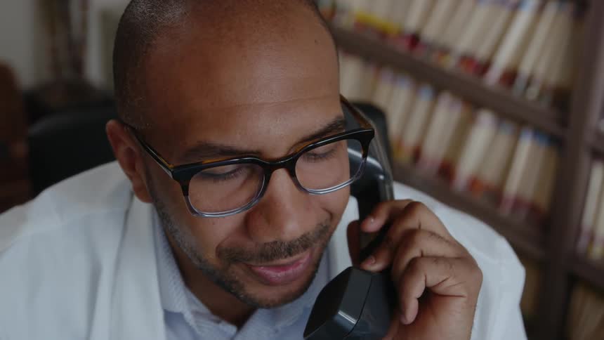 A man is talking on the phone and sitting in office