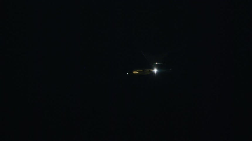 The lights on an airplane glow in the darkness as it flies low over town