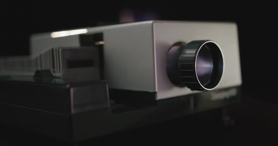 A projector device with a lens on the front sliding films in and out of the box
