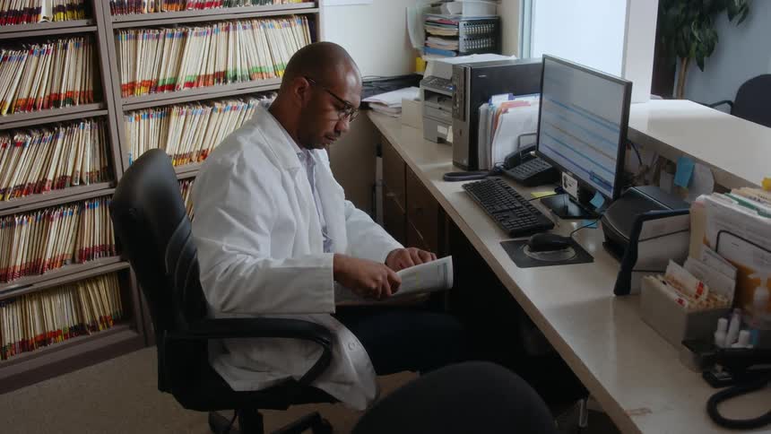A doctor at a counter checks a patient file then files it away in an archive