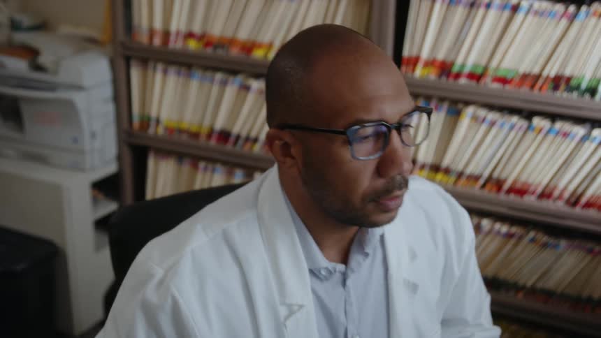 A male physician enters his office and sits down at his desk