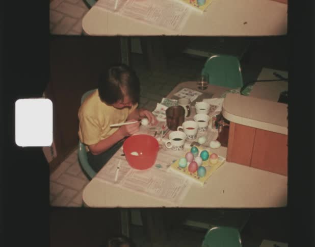 A young boy painting east eggs while sitting at a kitchen counter