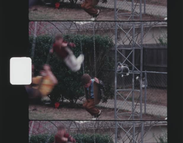 Vintage film of three young boys swinging on an outdoor swing set in a fencedoff yard
