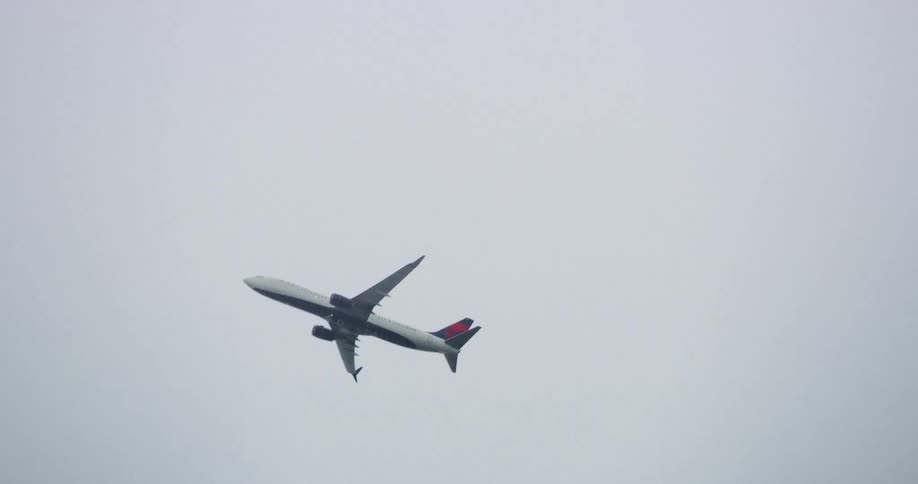 A commercial airplane flies across the cloudy sky until it disappears in the fog