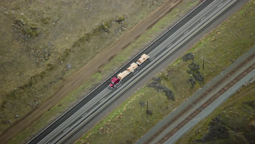 A semi truck hauling lumber is traveling on a road next to a railway