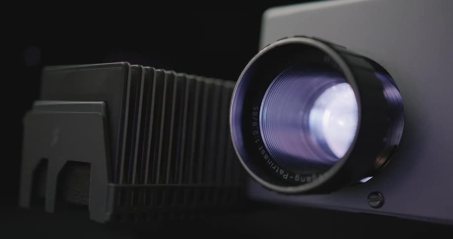 A slide projector shines light through its lens as it advances through slides