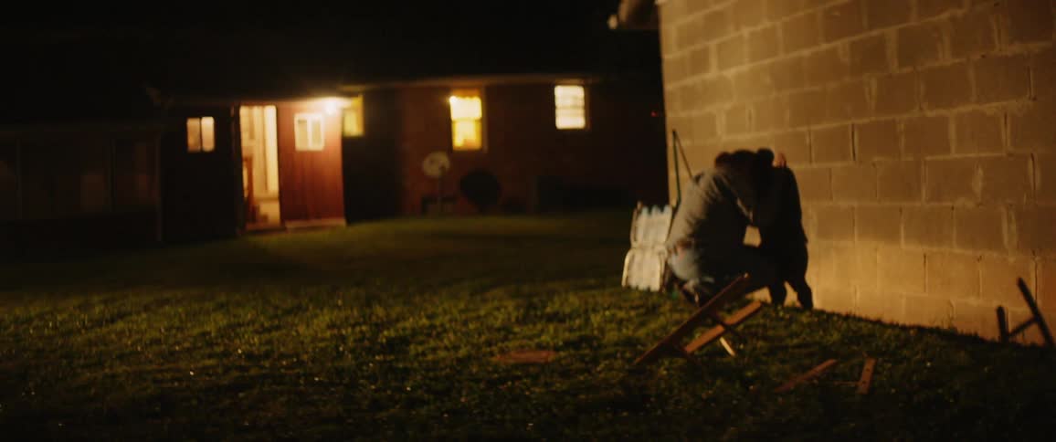 The man is leaning against the stone home at night