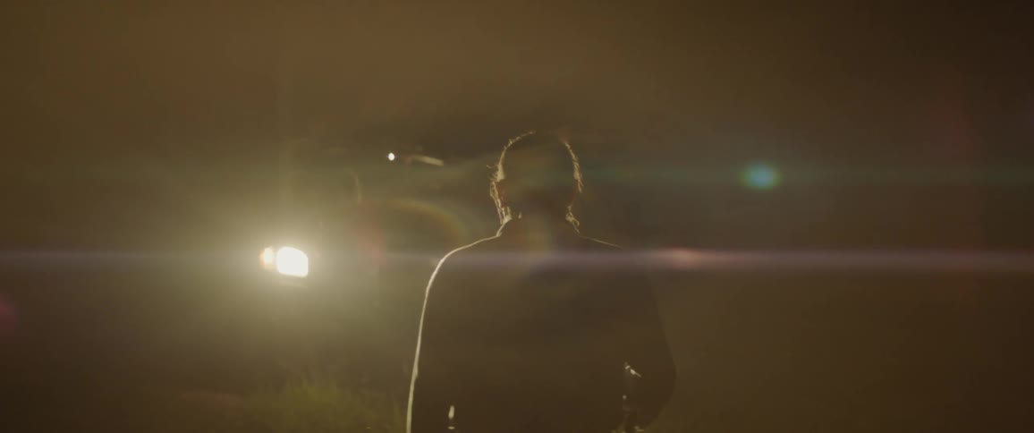 A man walks towards car headlights in a dark field