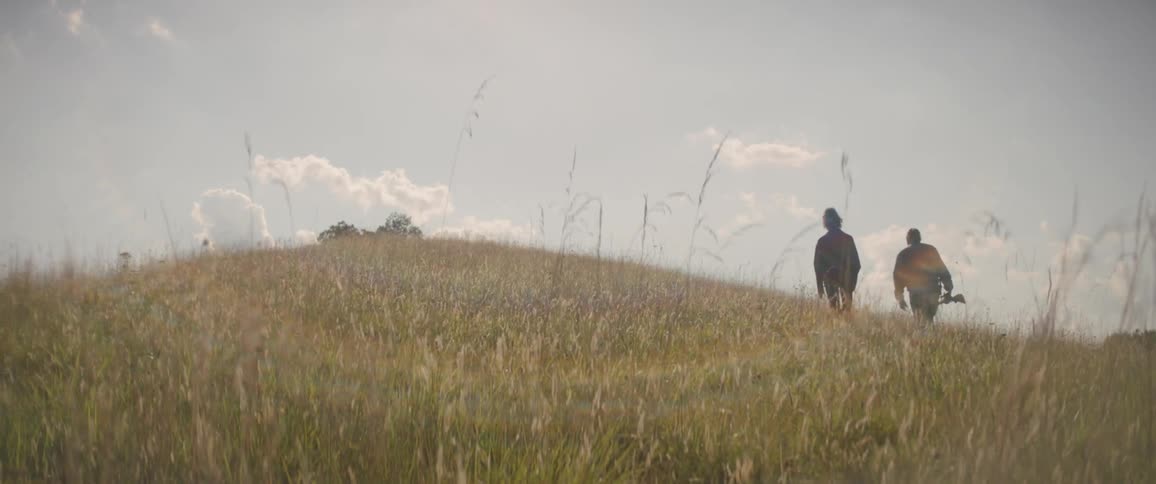 A man and woman walk on a grassy hill