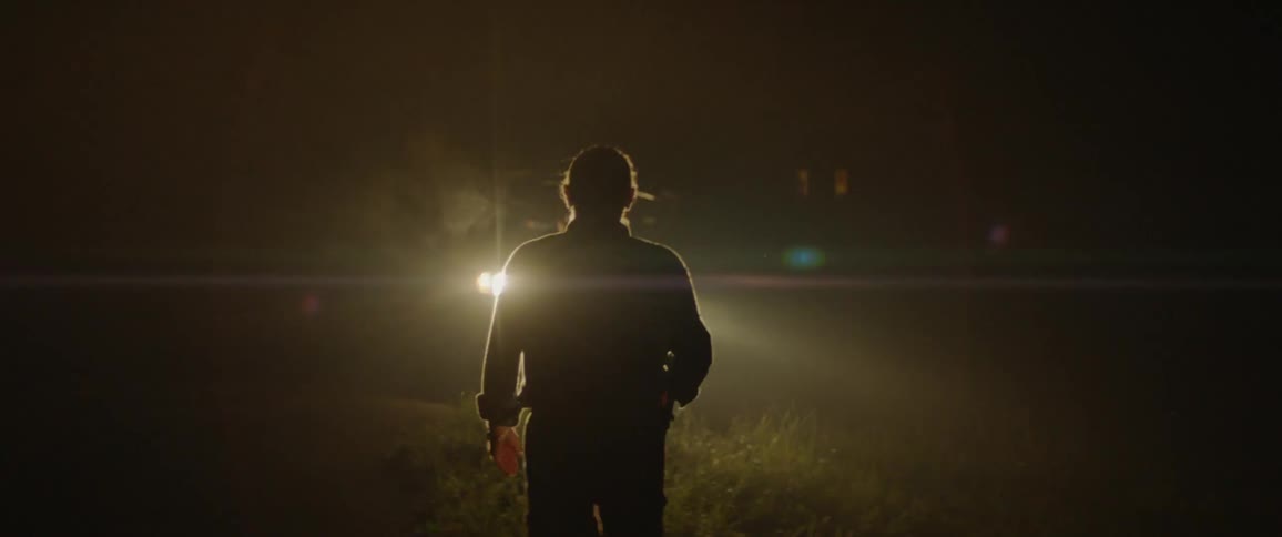 Man walks in the dark towards a vehicle with its headlights on