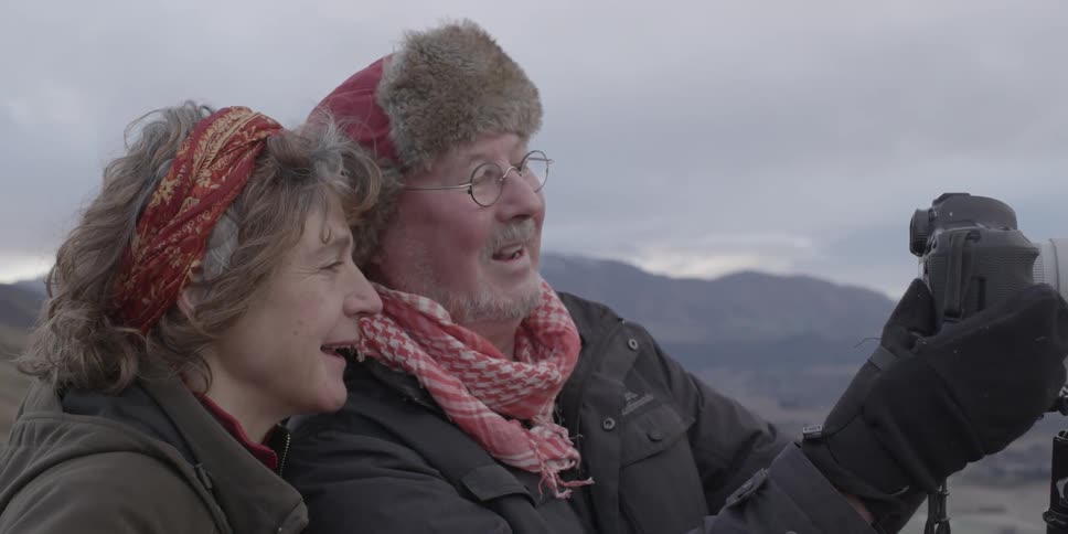 A man and a woman talking while looking at a camera