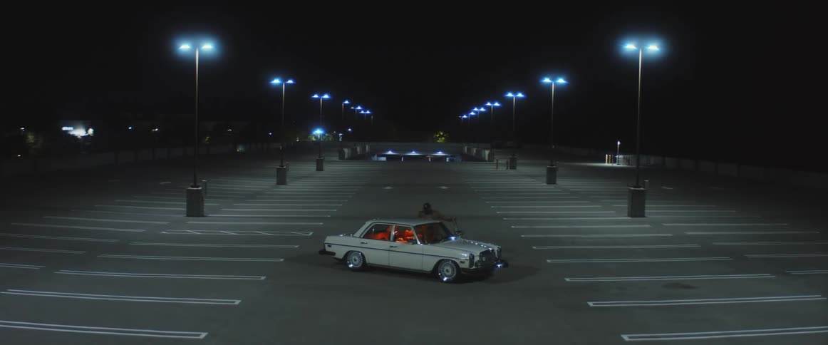 A man is parked alone on the upper level of a parking deck while waiting for someone at night