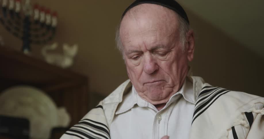 An old man dressed in jewish prayer shawl donning for morning prayer service