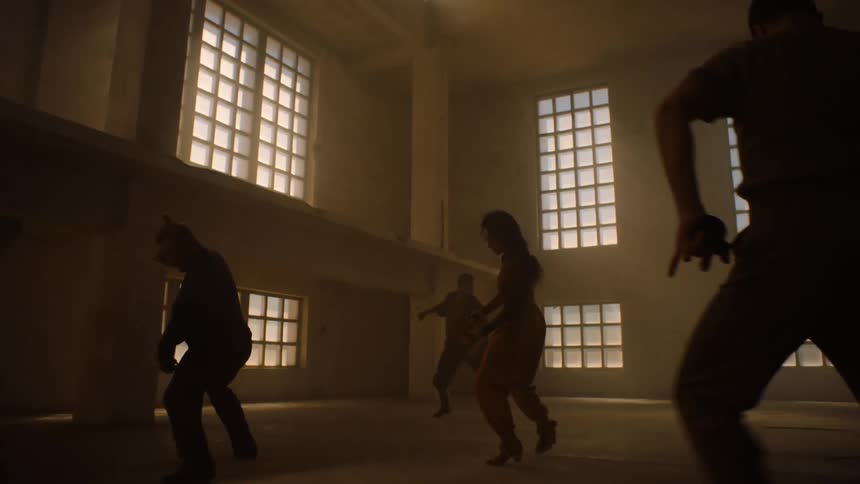 A group of dancers are in a room raising their arms in the air as they spin and move