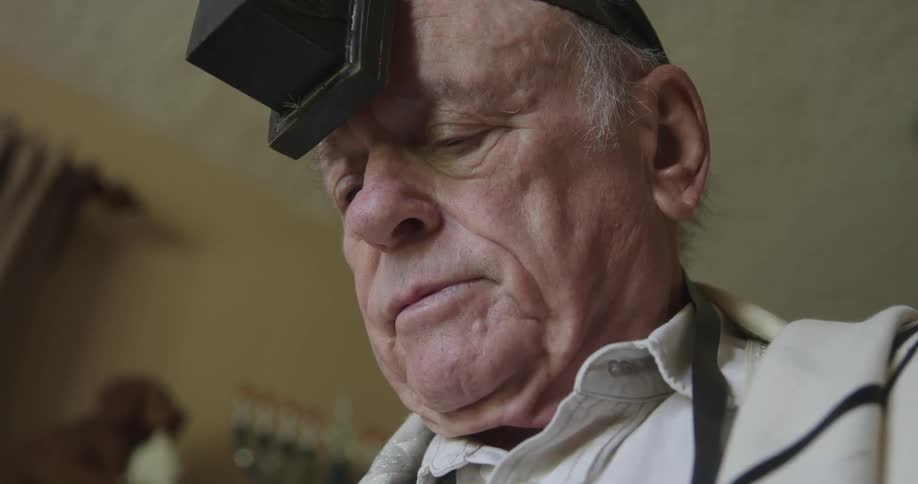 An older man is standing while looking down and reading while praying during the day