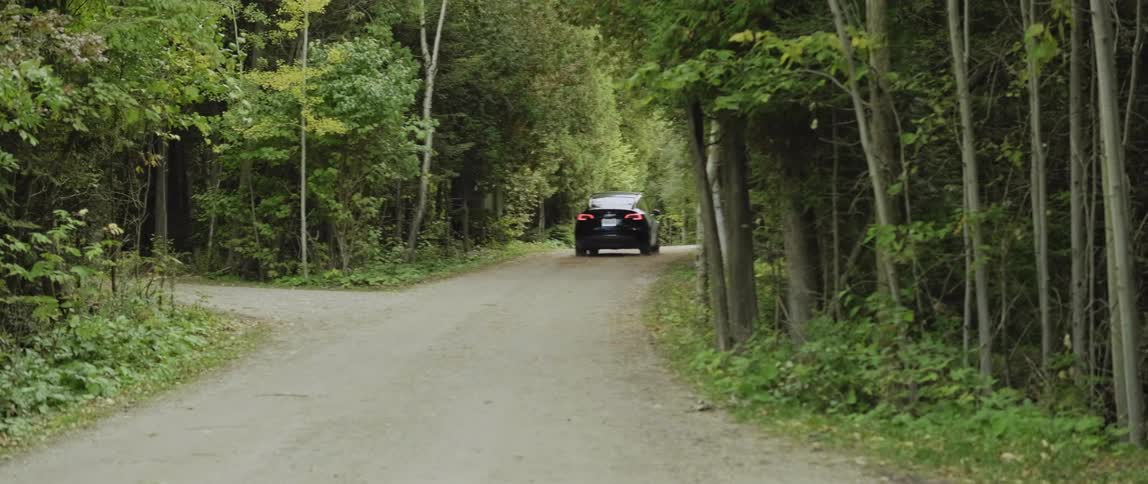 Black electric car drives on dirt road through green forest