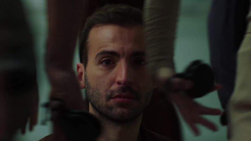 Close up of the face of a man sitting on the floor surrounded by people walking in circles aroudn him