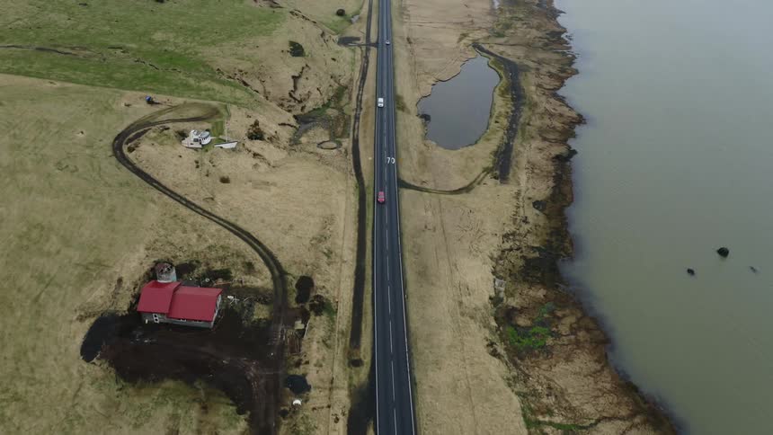 An aerial of a rural house near a coast line next to a road with traffic traveling on it