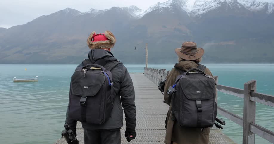 Two people walk along a boardwalk near a mountain