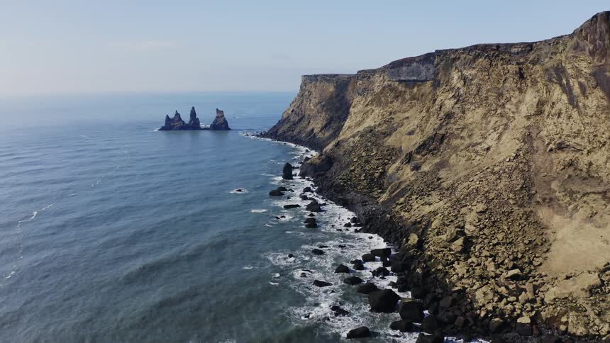 A drone view of a cliff on the coast line as ocean waves crash up against the rocks