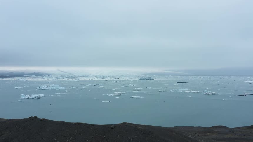 A rocky coastline giving way to the ocean filled with ice chunks and large ice caps