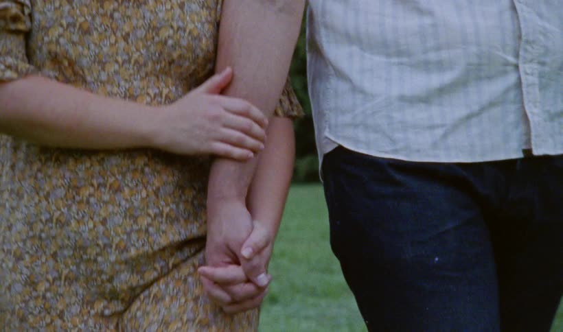 A man and woman holding hands while going for a stroll outside in summer