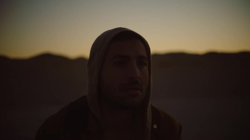 Man falls to his knees on ground with red sky topped mountains in the background