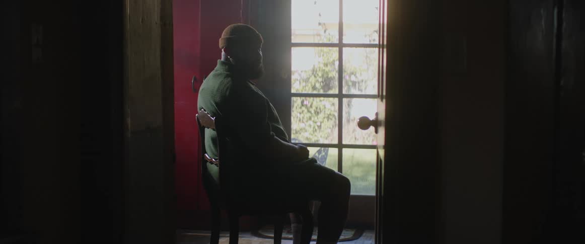 A man sitting in a chair in a room with the door open as sunlight shines through the window