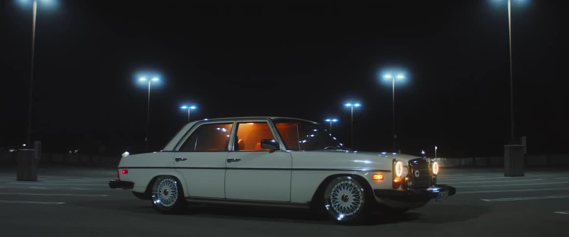 Old vehicle parked with headlights on in vacant parking lot at night