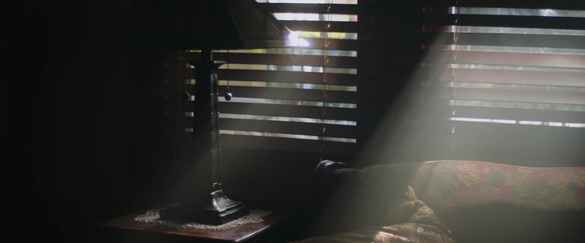 Light shines into a dark smoky room through the partially closed blinds