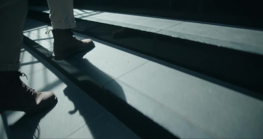 A close up of a persons feet walking up concrete steps outdoors casting a shadow behind them