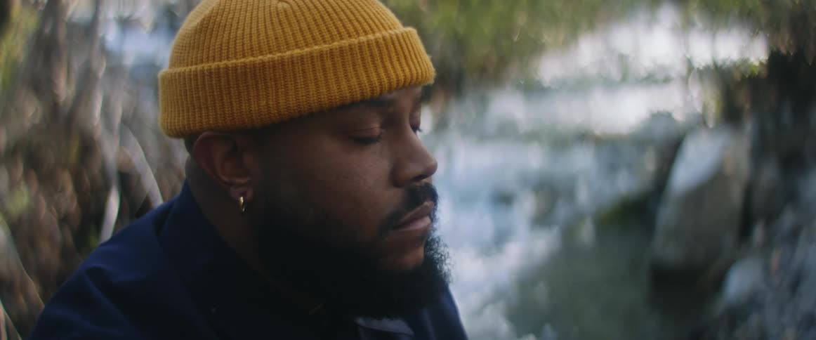 Man with yellow beanie beard and earrings sit by the stream