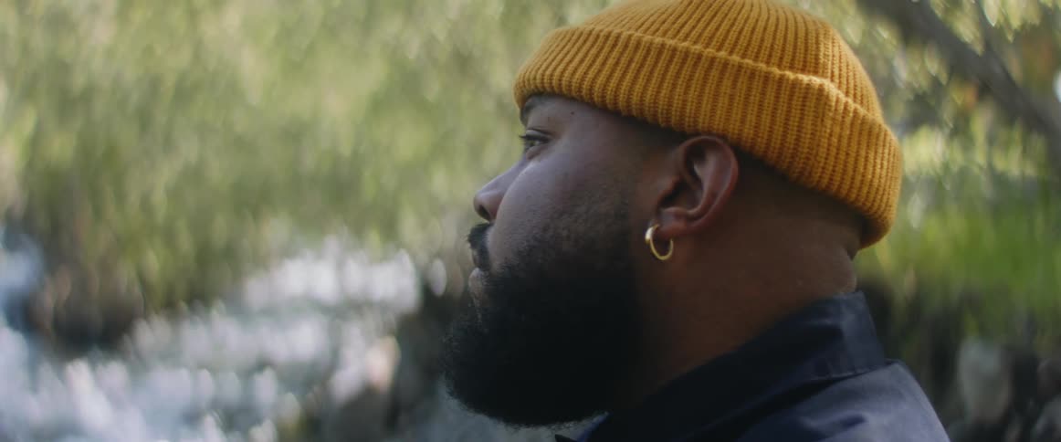 Bearded man wearing knit hat looks out over stream