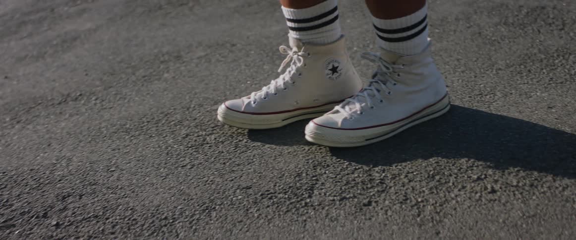 Two feet from the same person wearing converse shoes walk back as if preparing to start running soon