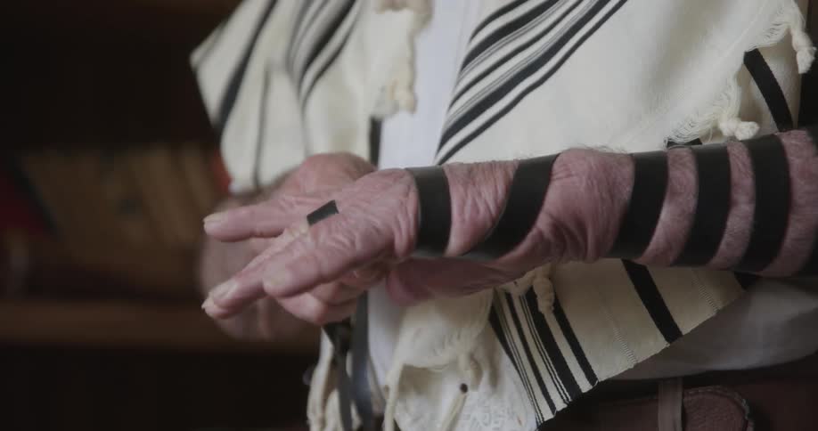 Close up of a jewish man wrapping a tefillin around his forearm before praying