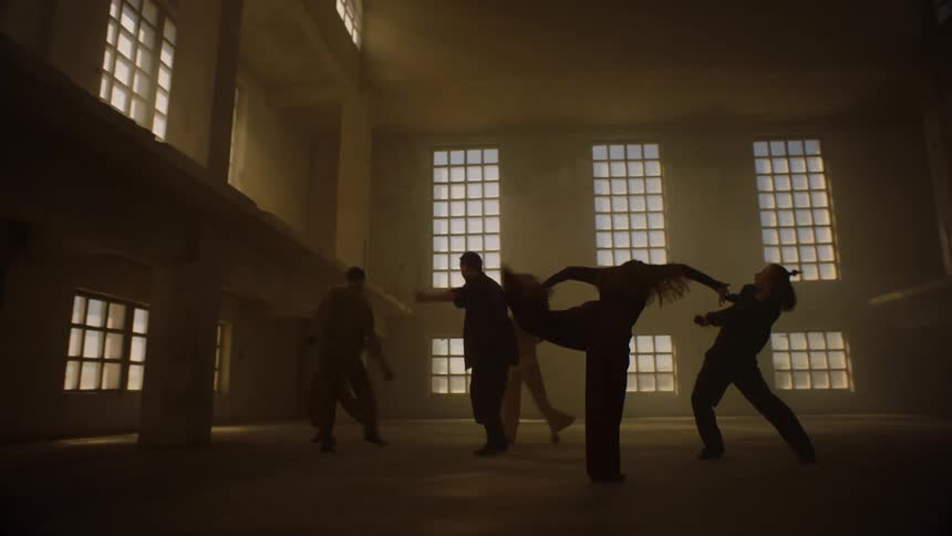 Female and male dancers dancing in building are silhouetted against the sun shining through windows