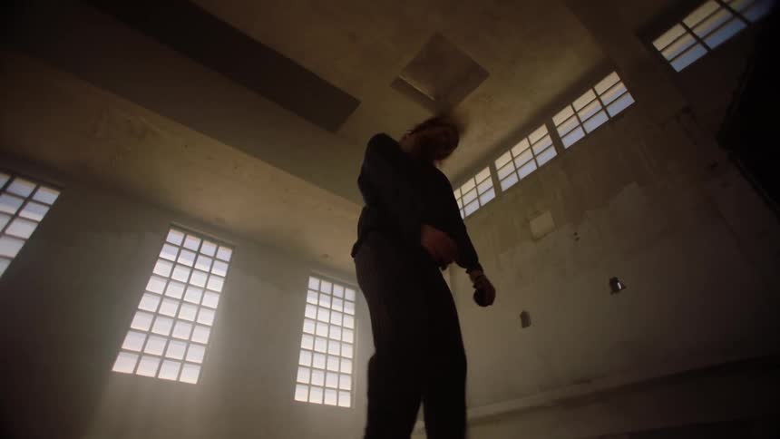 A man in black dances below light filled windows