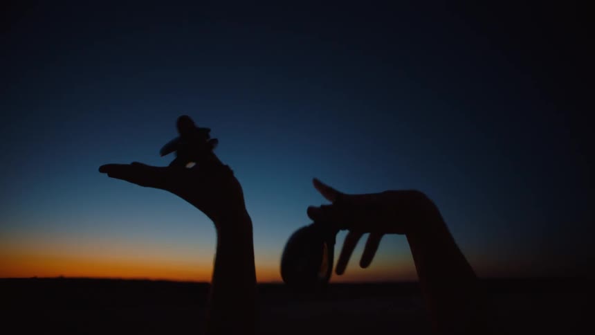 Close up of the silhouette of a couple hands holding castanets waving in the sky at evening