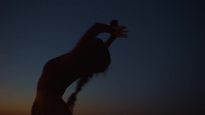 A silhouette of a woman dancing around in the dark under a night sky