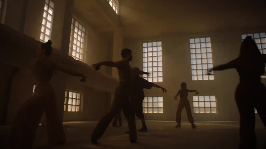 Dancers spin during a dance in dim room lit by tall windows