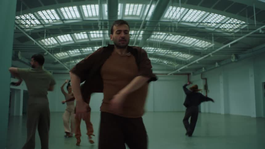 Dancers complete routine in large empty room lit by multiple skylights