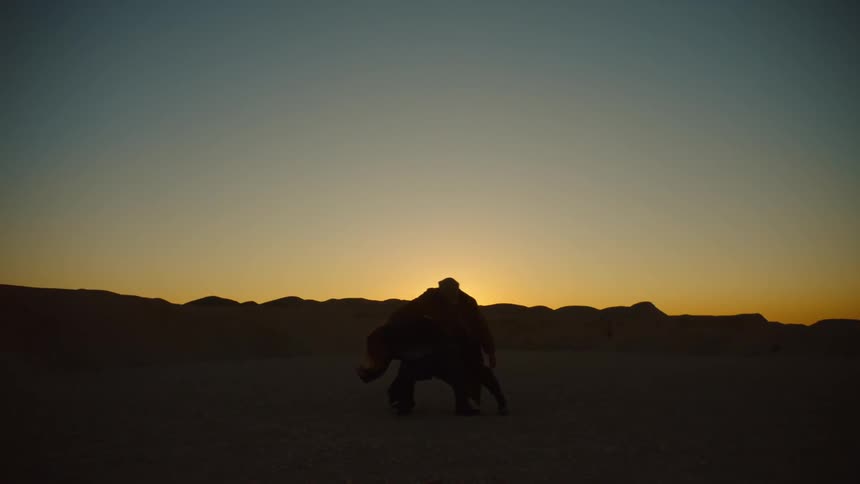 Two people dancing and moving in the desert at dusk as the sun sets