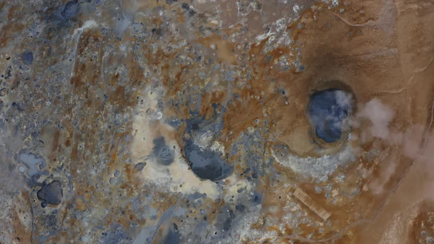 An aerial looking straight down on a rocky desert hot spring with steam coming off the water