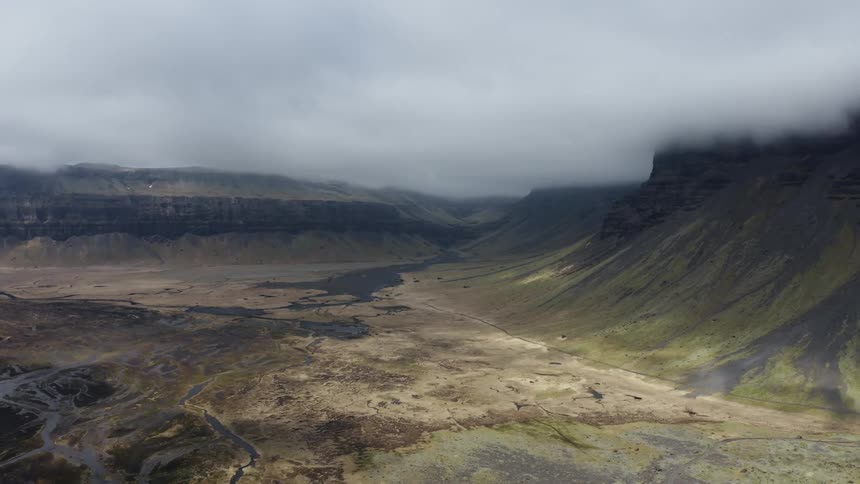 Rivers cross plain between mountains topped with low lying clouds