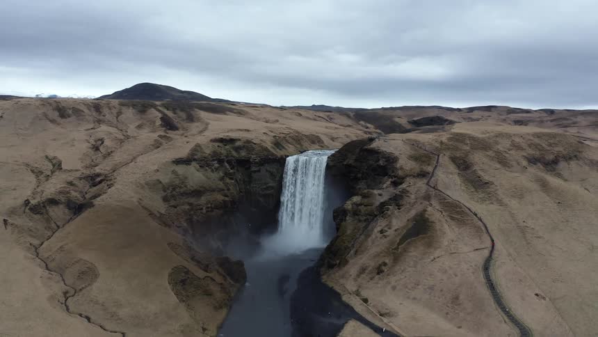 An aerial view of a wide waterfall on a barren landscape on a cloudy day