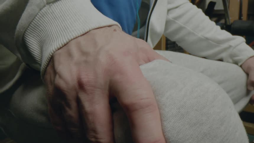 The hand of an old person grips his knee hard