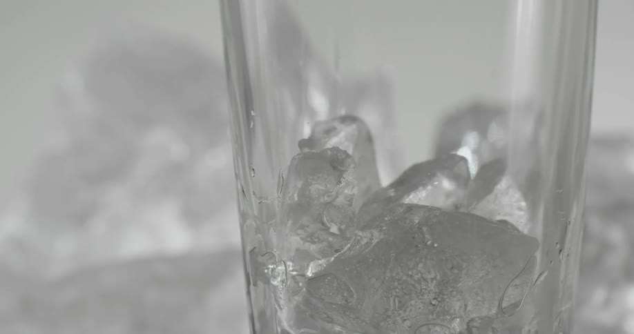 Ice cubes dropping into a clear glass on a table